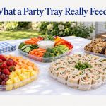 A buffet table with a fresh fruit tray, a vegetable tray with ranch dip, pinwheel wraps and a cookie platter, with the headline What a Party Tray Really Feeds